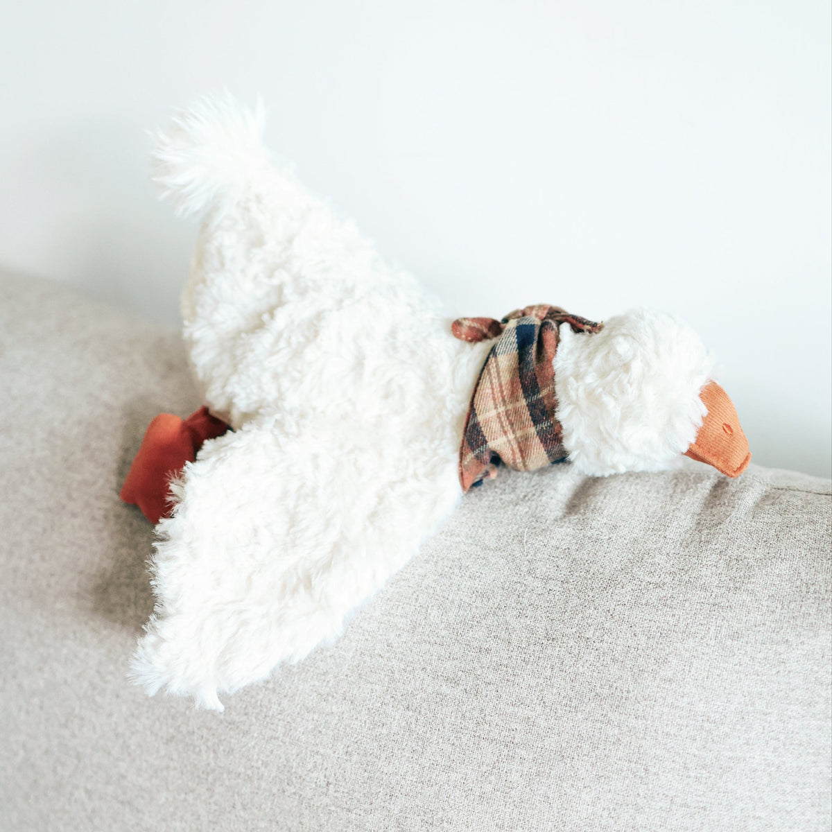 LAMBWOLF GUS – GUS Gans mit ausgebreiteten Flügeln auf dem Sofa